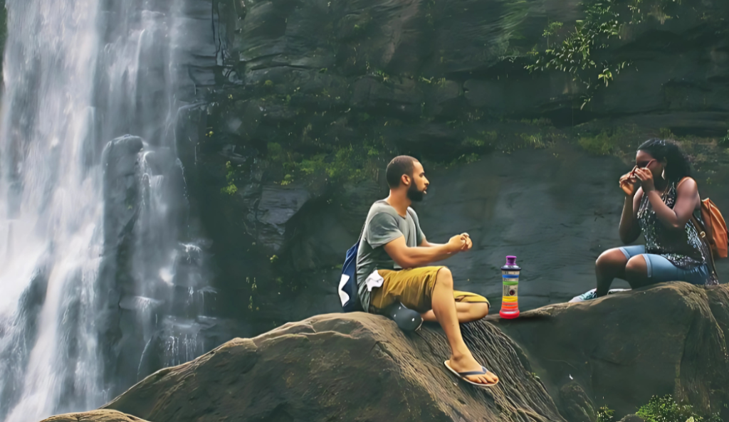 Couple sitting on rocks near a waterfall with an i9 Living Water Bottle, enjoying nature and eco-friendly hydration.